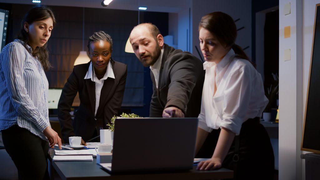 Présentation de la gestion de contrôle du travail d'équipe diversifié sur un ordinateur portable en train de réfléchir à des idées d'entreprise. Des hommes d'affaires multiethniques s'appuient sur une table de conférence dans une salle de réunion de bureau, tard dans la nuit.